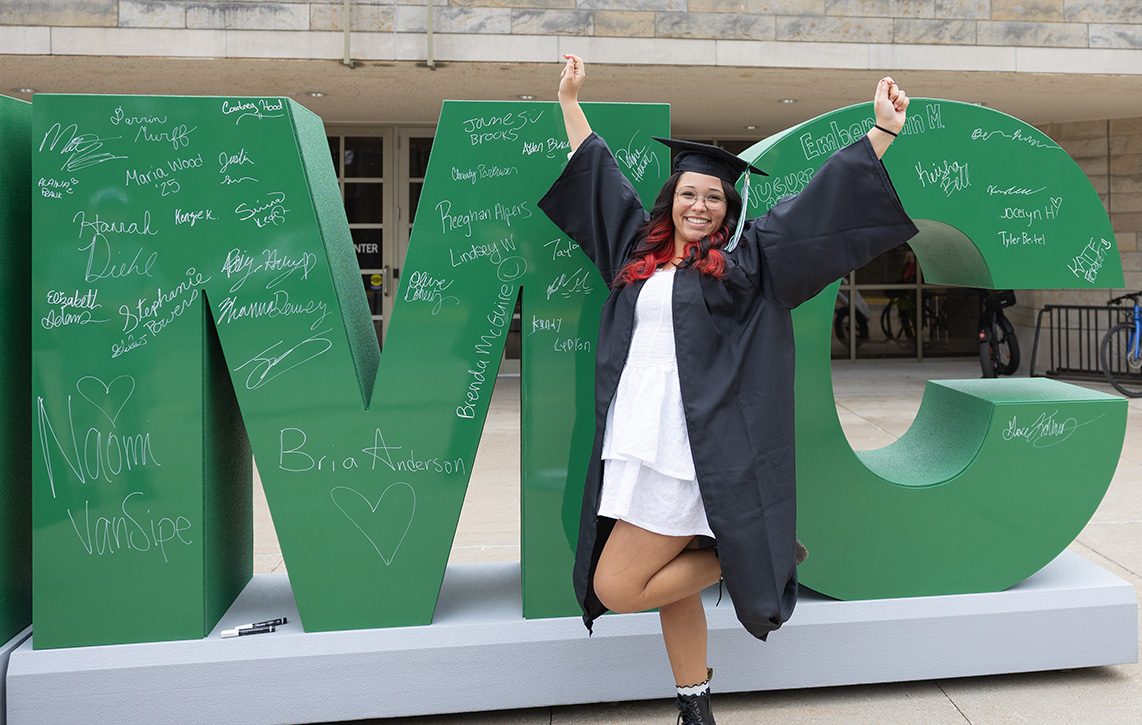 An NMC grad with her hands raised outside the 2025 Commencement ceremony