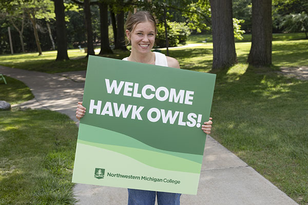 NMC residence advisor student holding a Welcome Hawk Owls sign