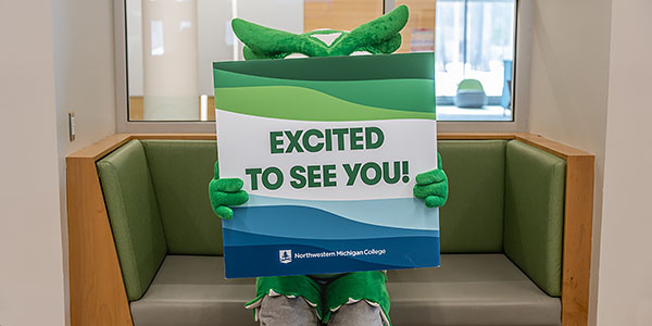 NMC's new mascot, Swoop, behind a sign that reads Excited to See You