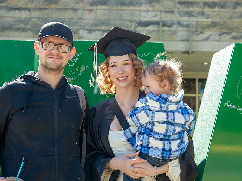 An NMC graduate poses outside the Dennos Museum Center after the 2026 Commencement ceremony